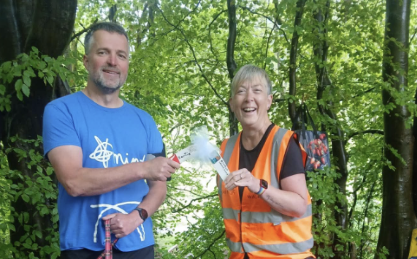 A man in a blue tee-shirt and a lady in a high-vis orange vest smile while holding a boomerang.