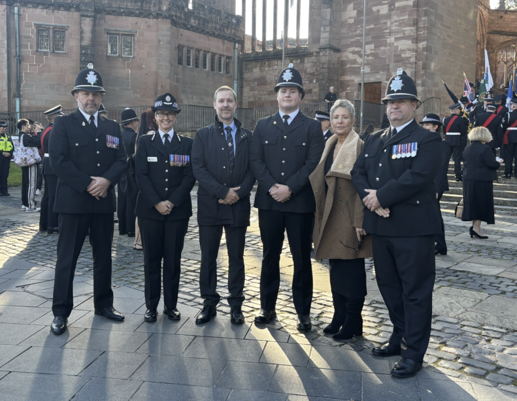 A group of Northumbria Police Federation members and police officers in full uniform stand with members of the public against the backdrop of Coventry Cathedral