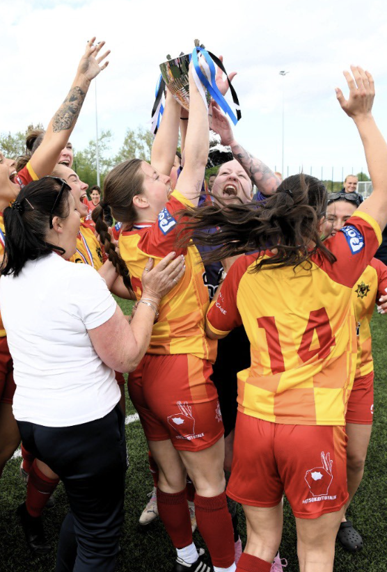 A group of 5 women footballers cheer and lift the PSUK trophy